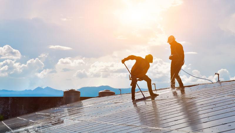 Two people cleaning solar panels on the roof of a house